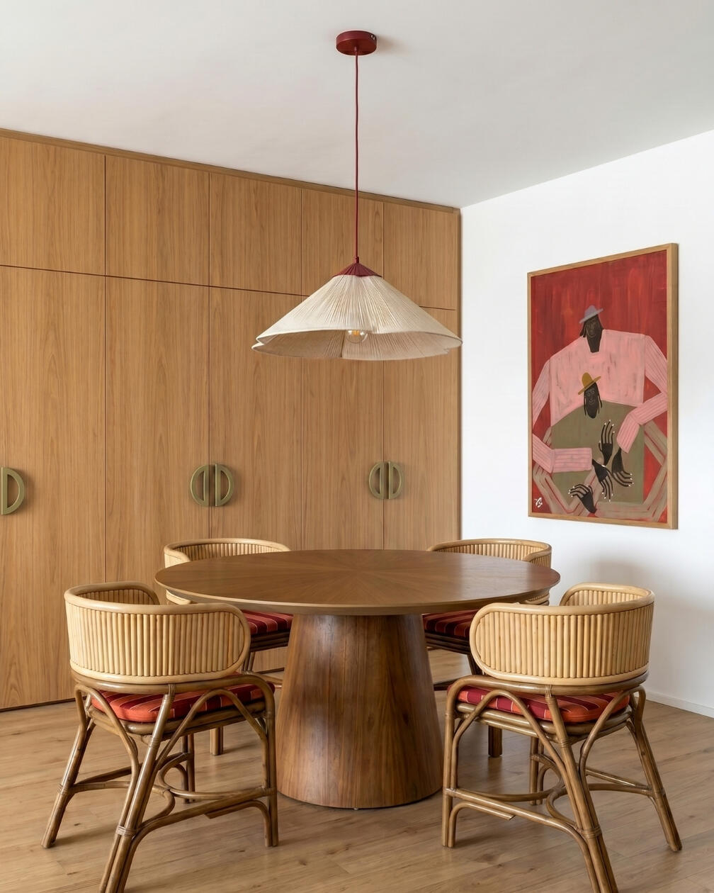 A madeira como elemento central de uma sala de jantar quente, descontraída e intemporal. Sala de jantar com mesa redonda em madeira, quatro cadeiras em fibras naturais, candeeiro suspenso e parede revestida a madeira.