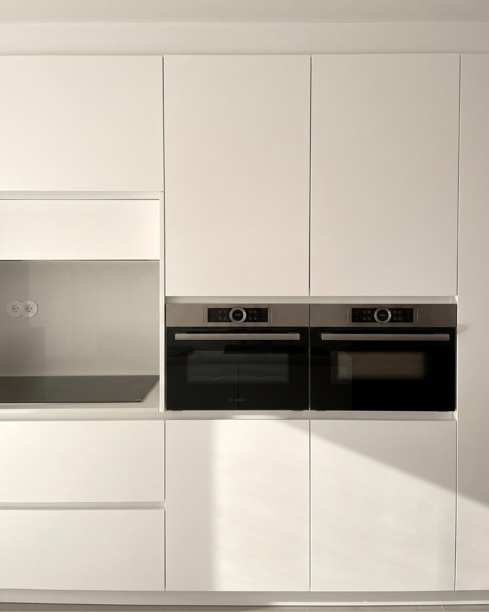 Uma cozinha de linhas depuradas e arquitetura simples. Cozinha contemporânea com armários brancos de linhas lisas, eletrodomésticos integrados e bancada clara.