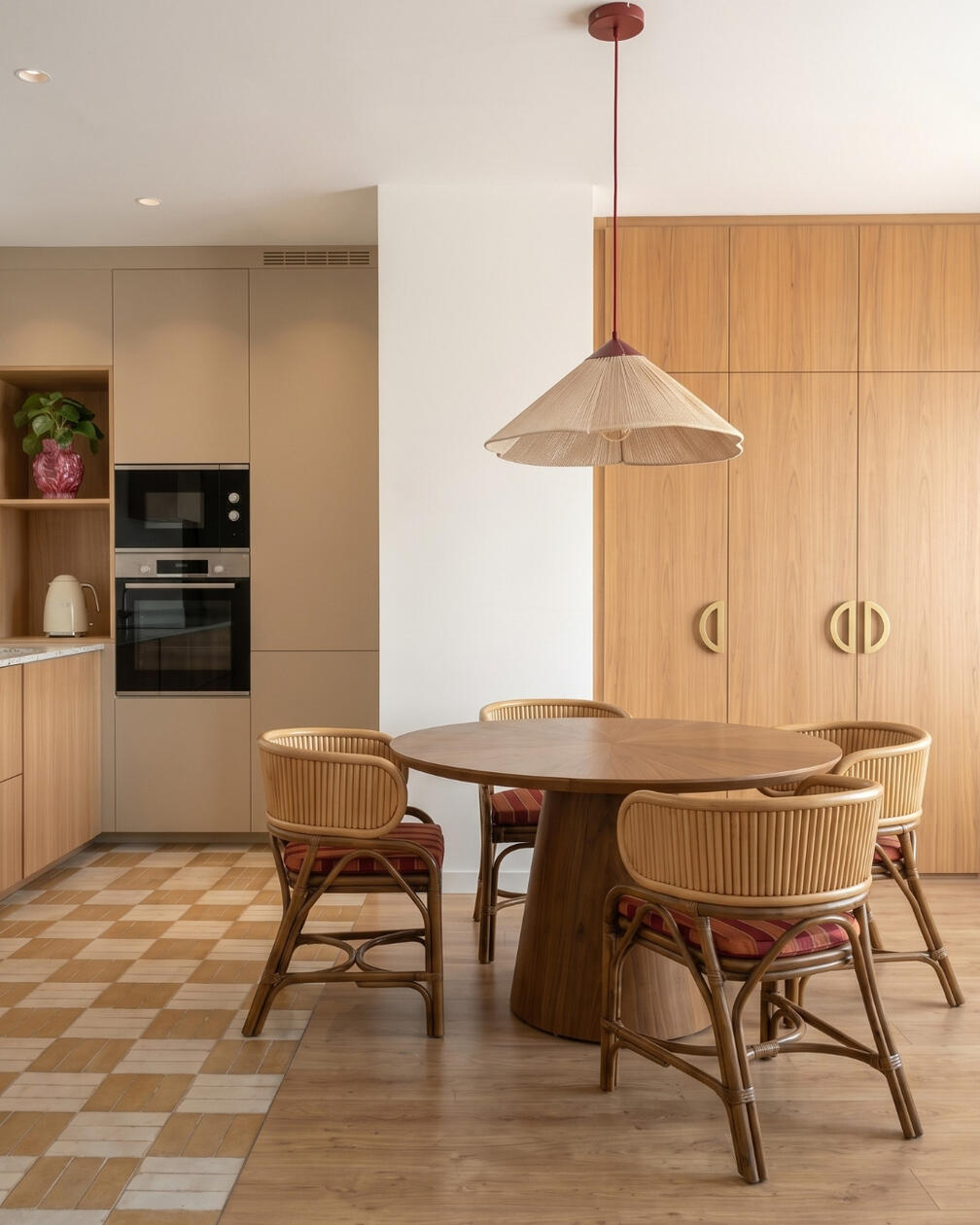 Uma composição descontraída onde a madeira e o padrão do pavimento dão identidade ao espaço. Sala de jantar com mesa redonda em madeira, cadeiras em fibras naturais, cozinha em madeira e pavimento com padrão geométrico.